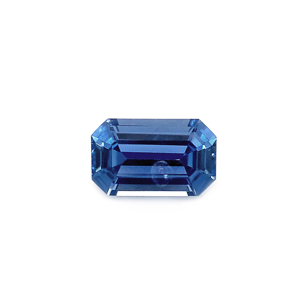 An emerald-cut unheated Yogo sapphire with a mirror-like facets reflecting light, presenting a deep blue color.