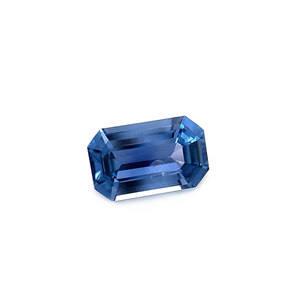 Angled view of an emerald-cut unheated Yogo sapphire with a mirror-like facets reflecting light, presenting a deep blue color.