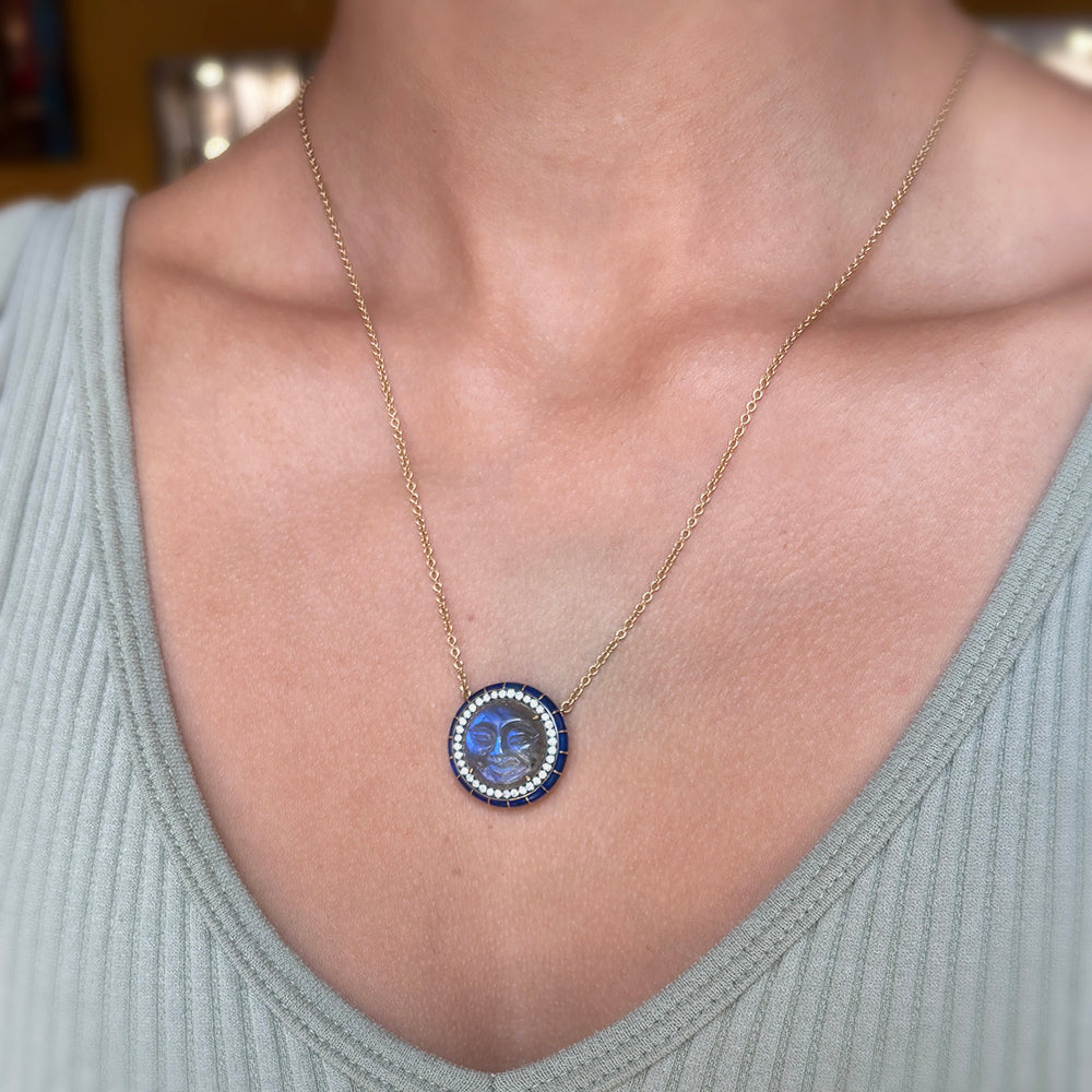 Necklace with a blue man in the moon pendant worn by a person in a light gray top.