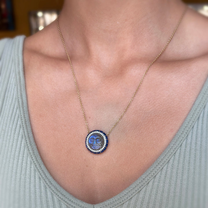 Necklace with a blue man in the moon pendant worn by a person in a light gray top.