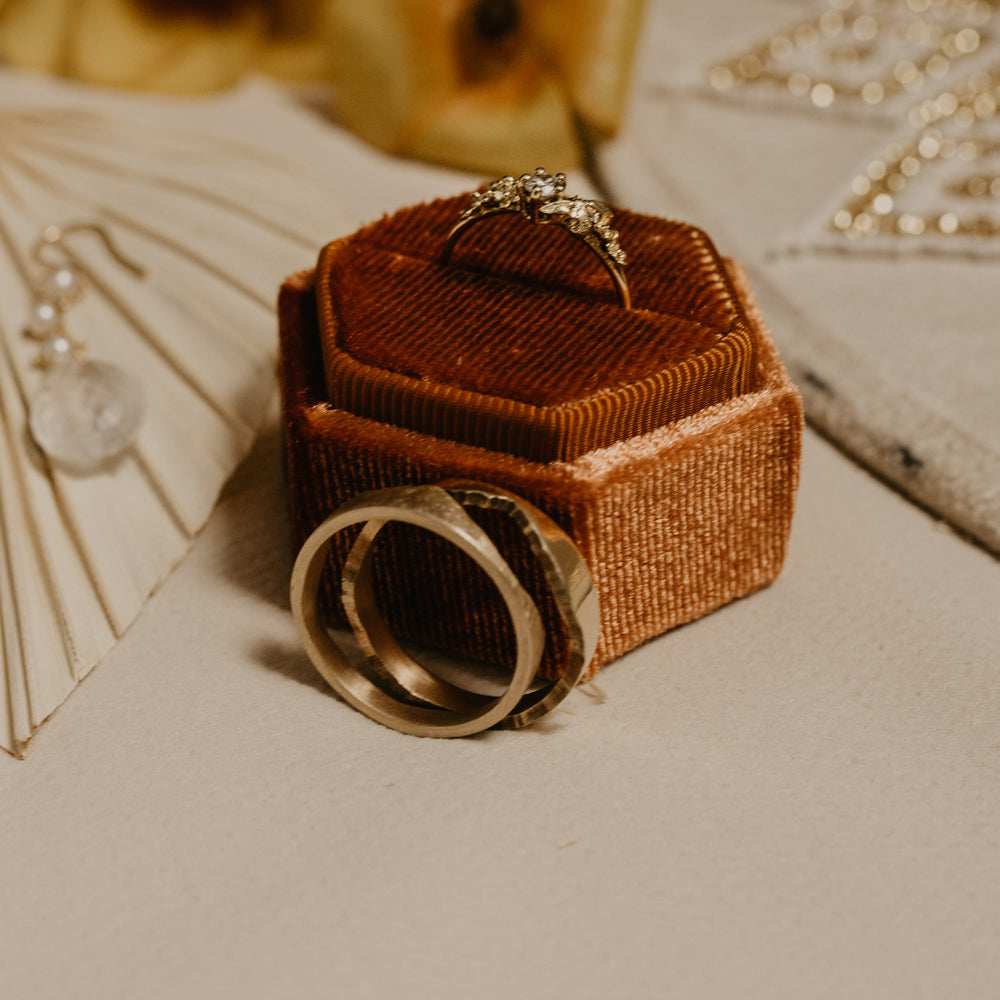 Alex Monroe diamond engagement ring in a ring box, plus men's wedding band by Hannah Louise Lamb showing a Montana river outline.