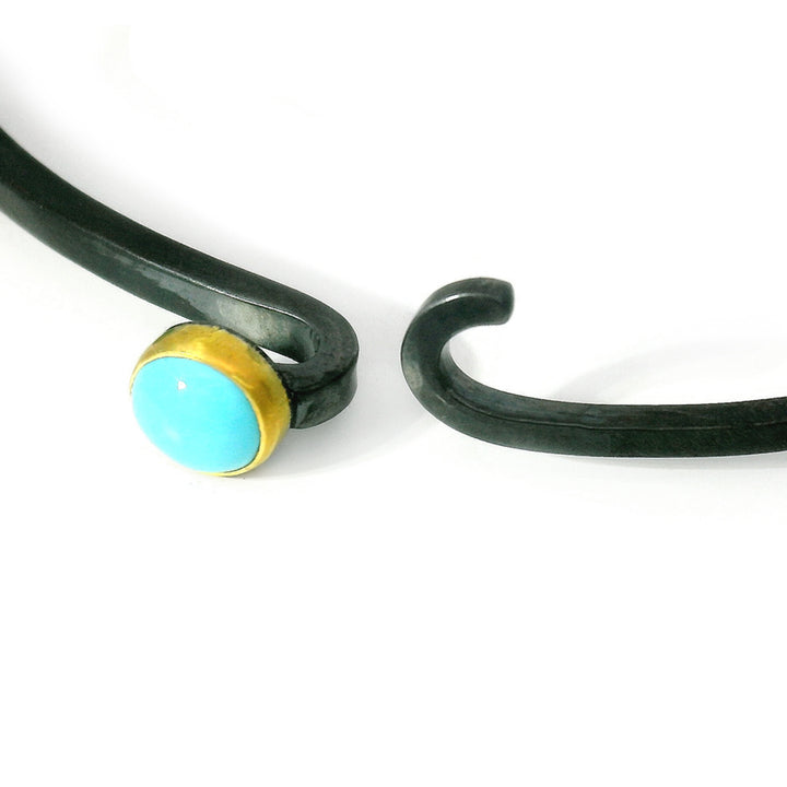 Close-up of round turquoise cabochon set in gold bezel on silver hook bracelet
