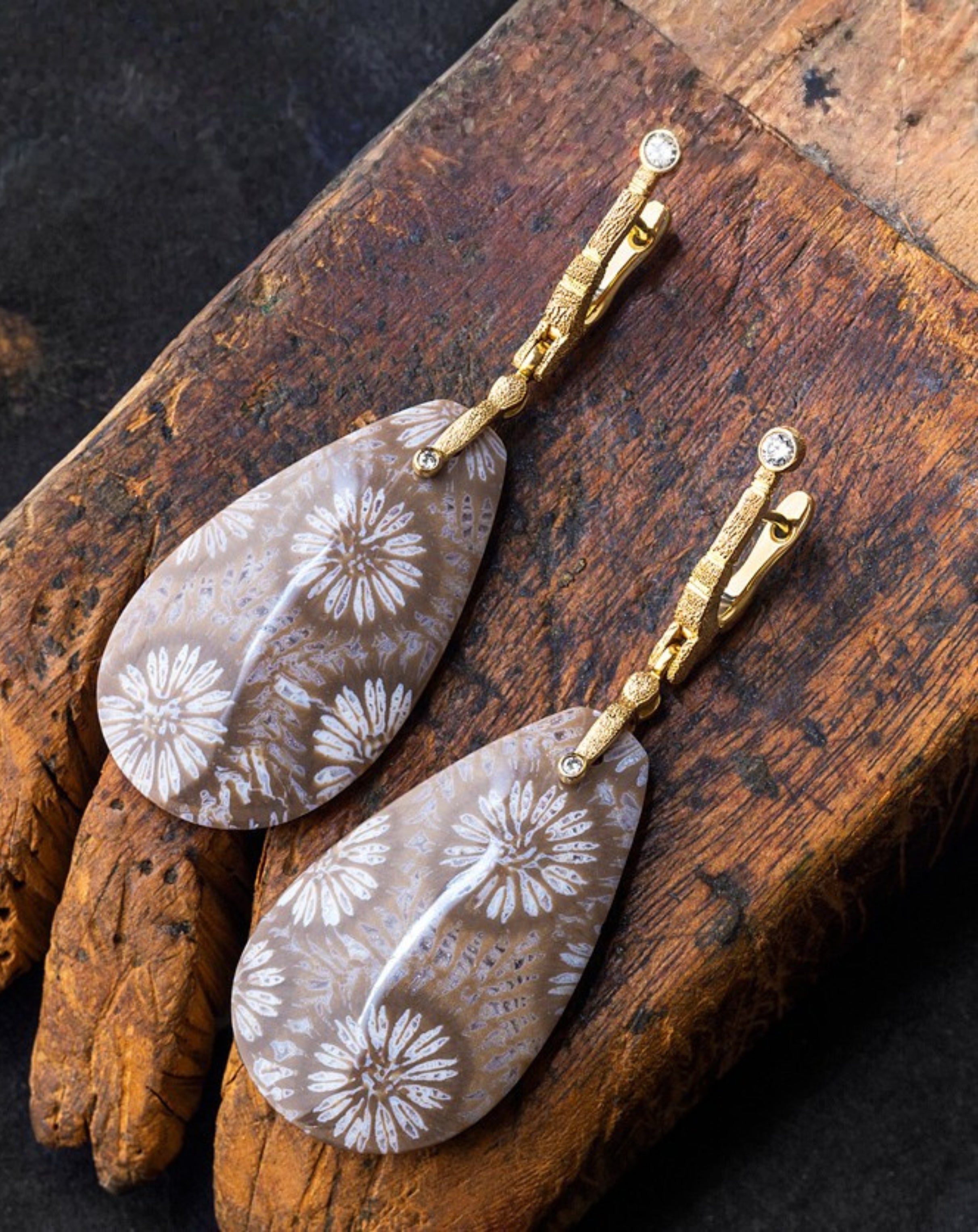 A pair of Alex Sepkus Sticks and Stones drop earrings with fossilized coral drops, hanging from textured gold leverback clasps with small diamonds, displayed on a rustic wooden block.