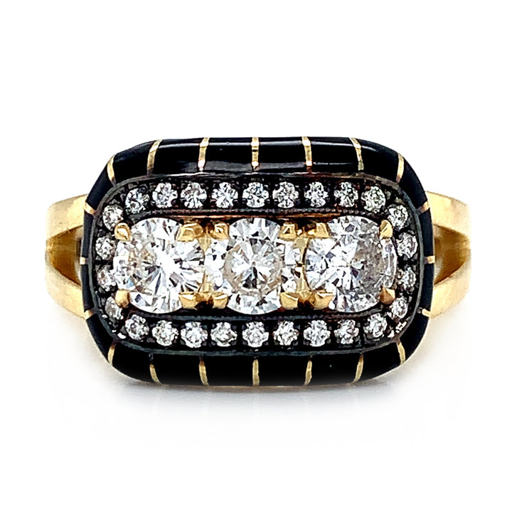 A ring featuring a halo of round diamonds surrounding three larger center brilliant-cut diamonds set in 18k yellow gold with black enamel detailing.