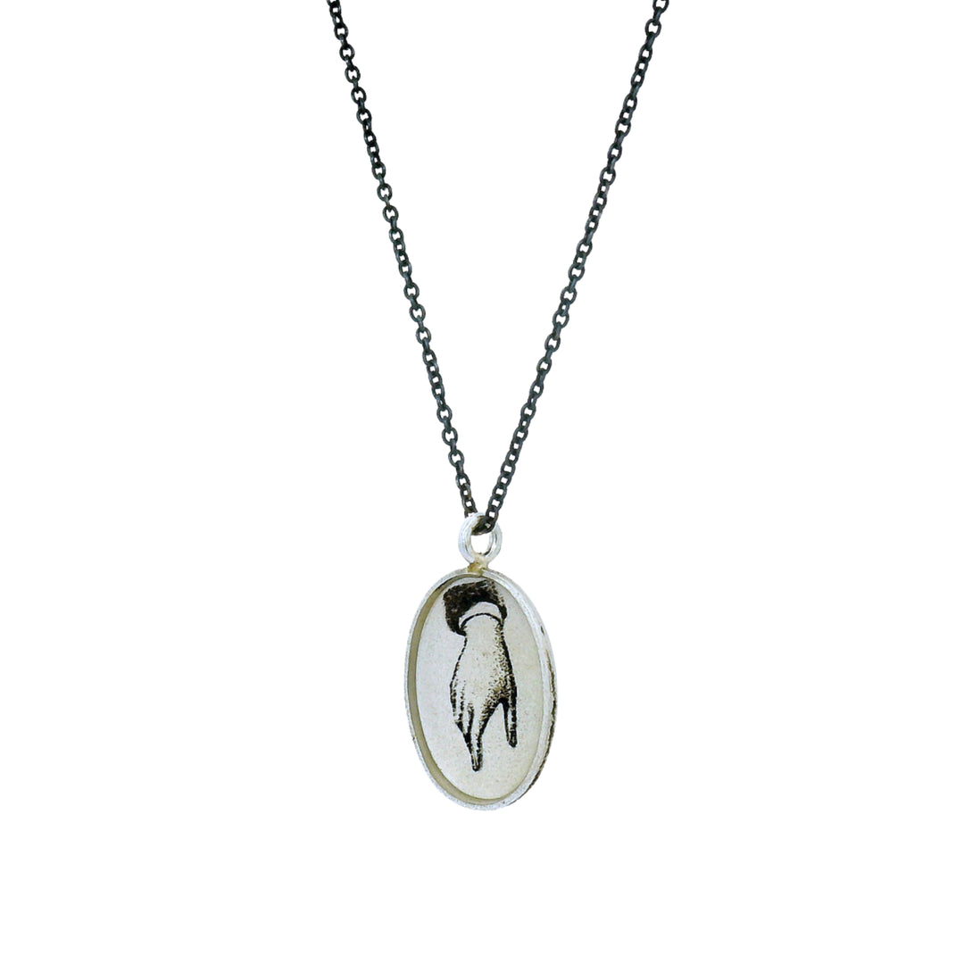 Close-up of etched hand illustration on oval sterling silver pendant