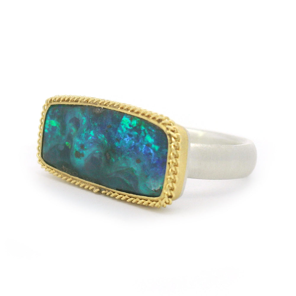 silver ring with a gold bezel holding and dark blue and green boulder opal